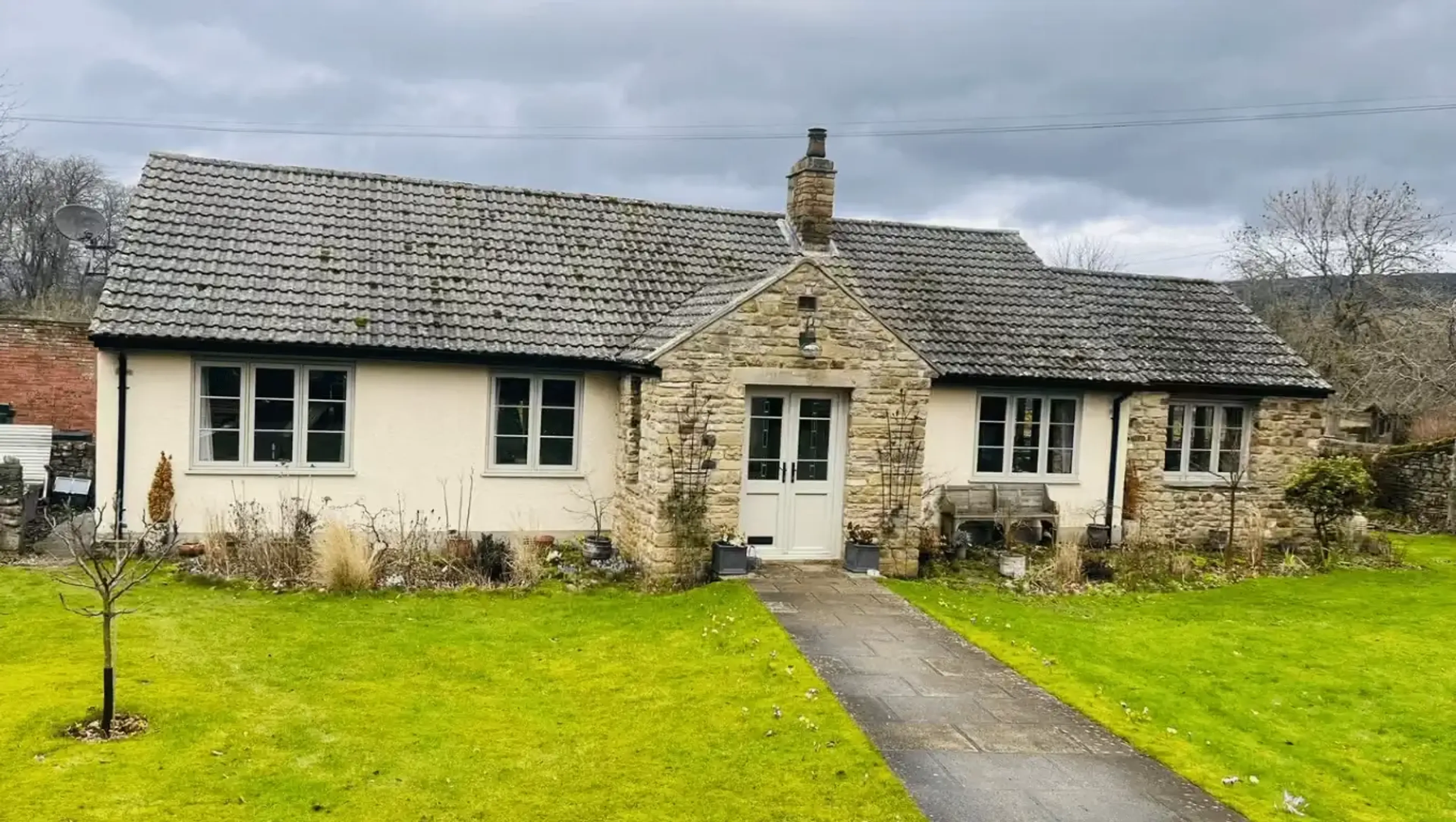 Stone bungalow with new uPVC windows and doors installed by Starlight Windows, featuring casement windows and a white front door with a landscaped front garden